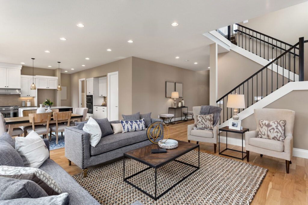 A large, open basement with neutral walls, carpeted flooring, a modern kitchenette with dark cabinets, and ample space for recreation or additional living areas.