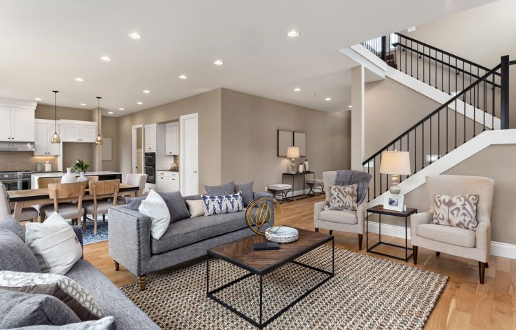 A large, open basement with neutral walls, carpeted flooring, a modern kitchenette with dark cabinets, and ample space for recreation or additional living areas.