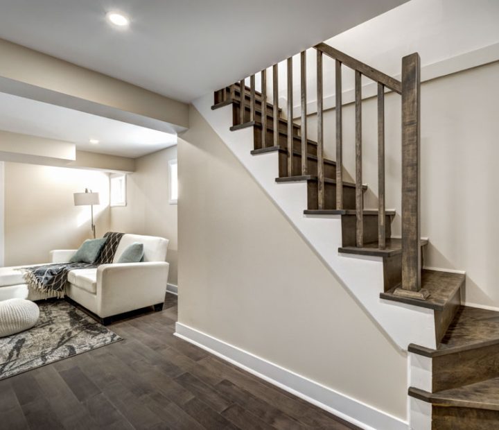 A minimalist interior featuring a staircase with dark wood treads and railings, white walls, and a cozy seating area below, blending rustic and contemporary design.