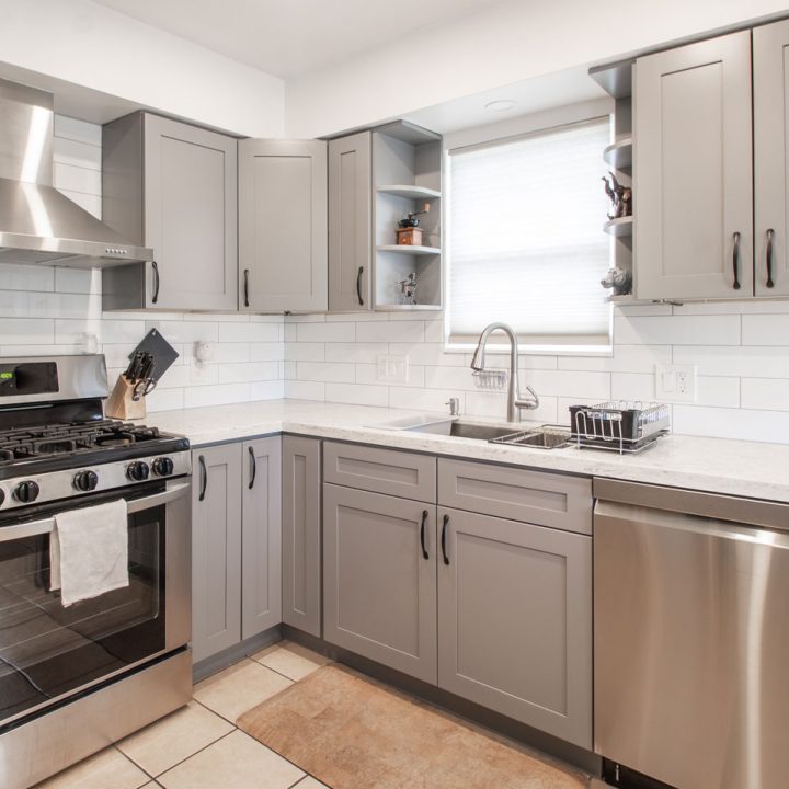 A clean, well-lit kitchen with gray cabinets, white subway tile backsplash, stainless steel appliances, a gas range, and a double sink under a window, offering a practical and stylish design.